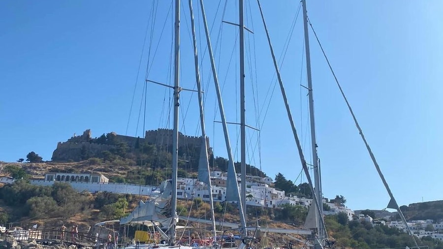 Sailing yacht masts rise in the bay below the Acropolis of Lindos and its white houses on a Rhodes yacht cruise