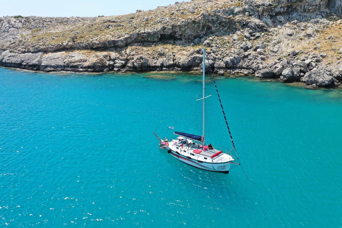 Rhodes yacht cruise sailing yacht at anchor in a turquoise bay below a rocky coast