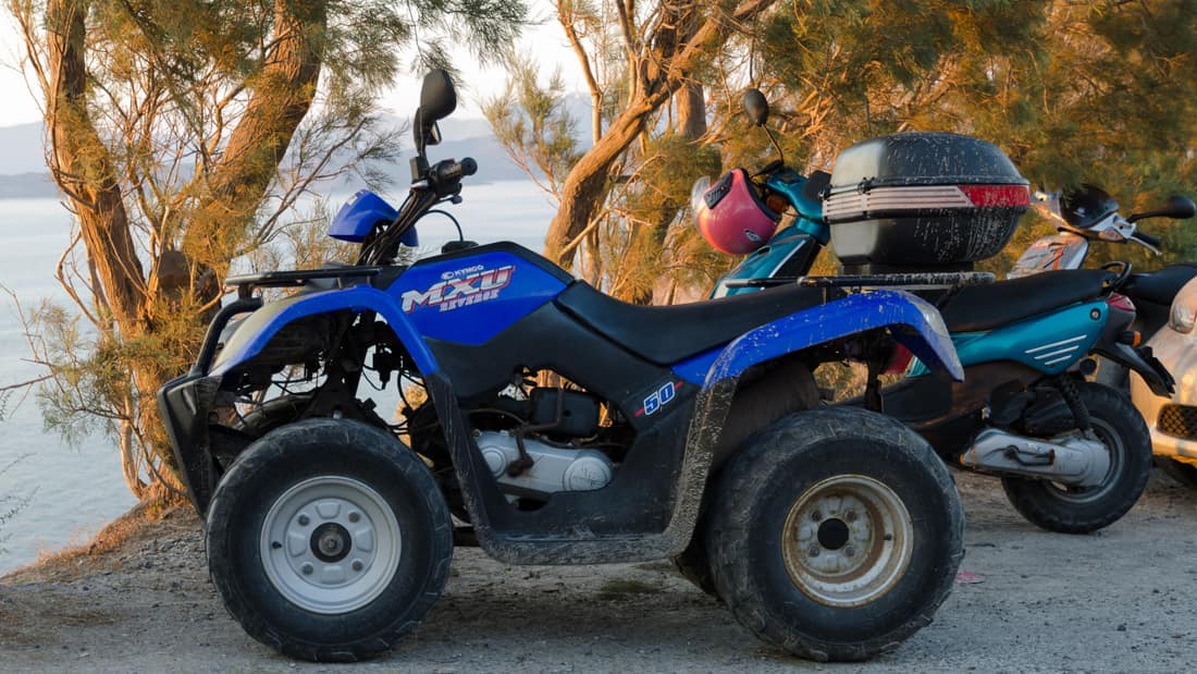 A Santorini ATV tour sets off on a four-wheeled quad parked under the trees by the sea