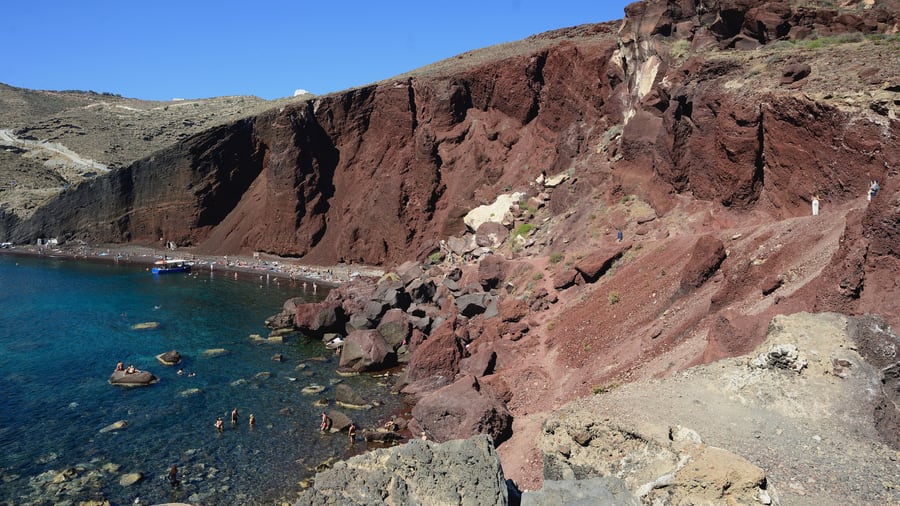 A Santorini ATV tour reaches Red Beach, where red volcanic cliffs drop to a narrow strip of sand