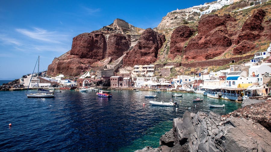 A Santorini boat tour leaves from Ammoudi Bay below Oia, between red volcanic cliffs and fishing boats