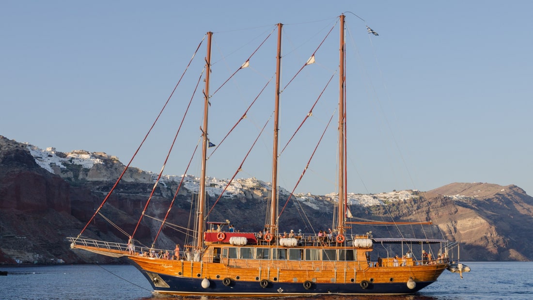 A Santorini boat tour sails a tall wooden ship across the caldera below the white houses of Oia