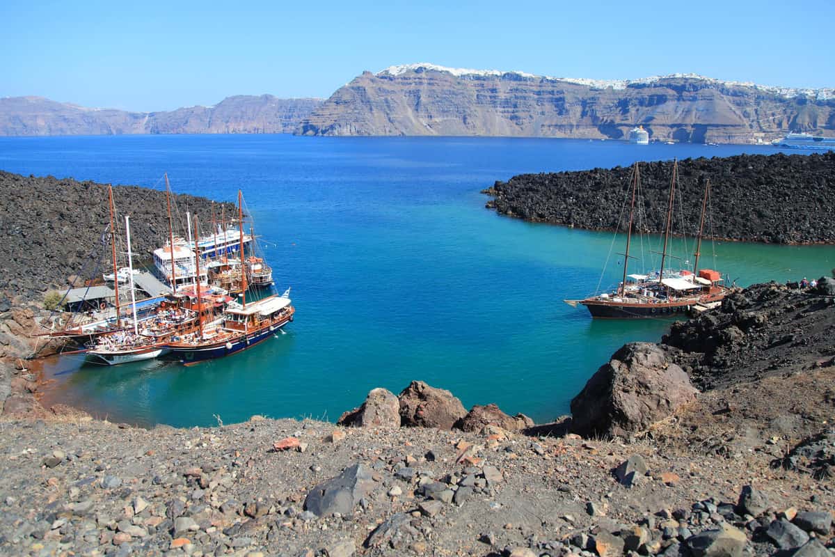 Santorini boat trip wooden boats moored in a blue cove of Nea Kameni, with the caldera cliffs behind