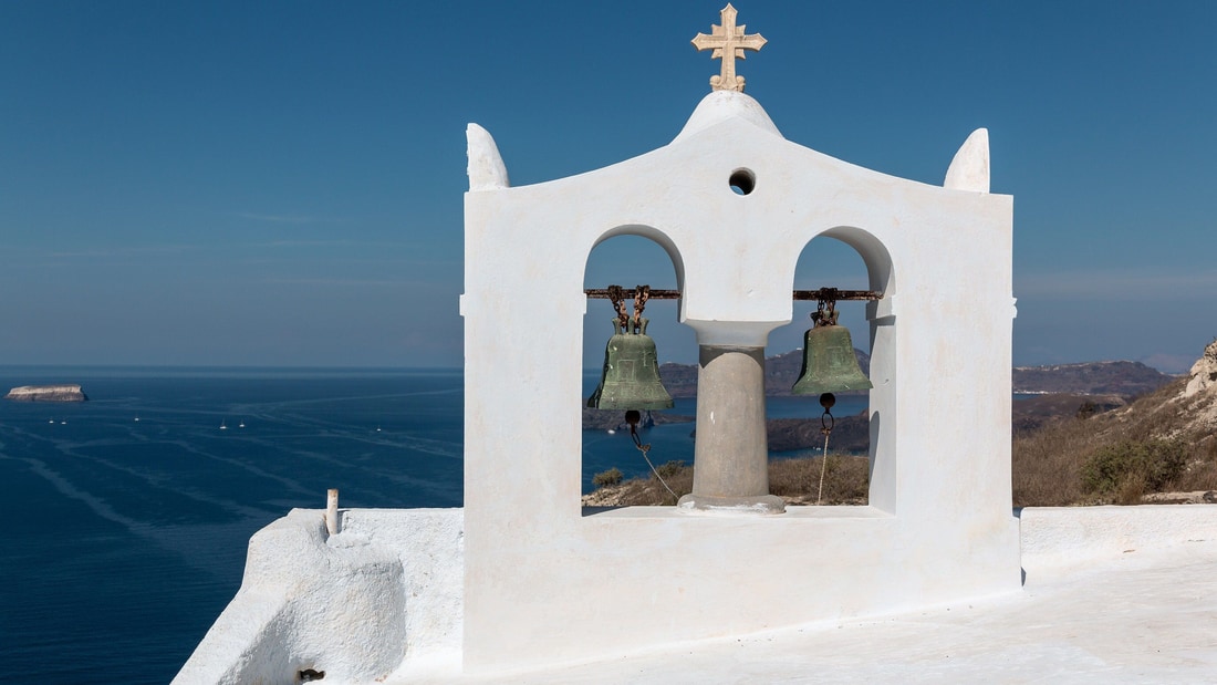 A Santorini food tour passes the white bell tower of Megalochori above the blue water of the caldera