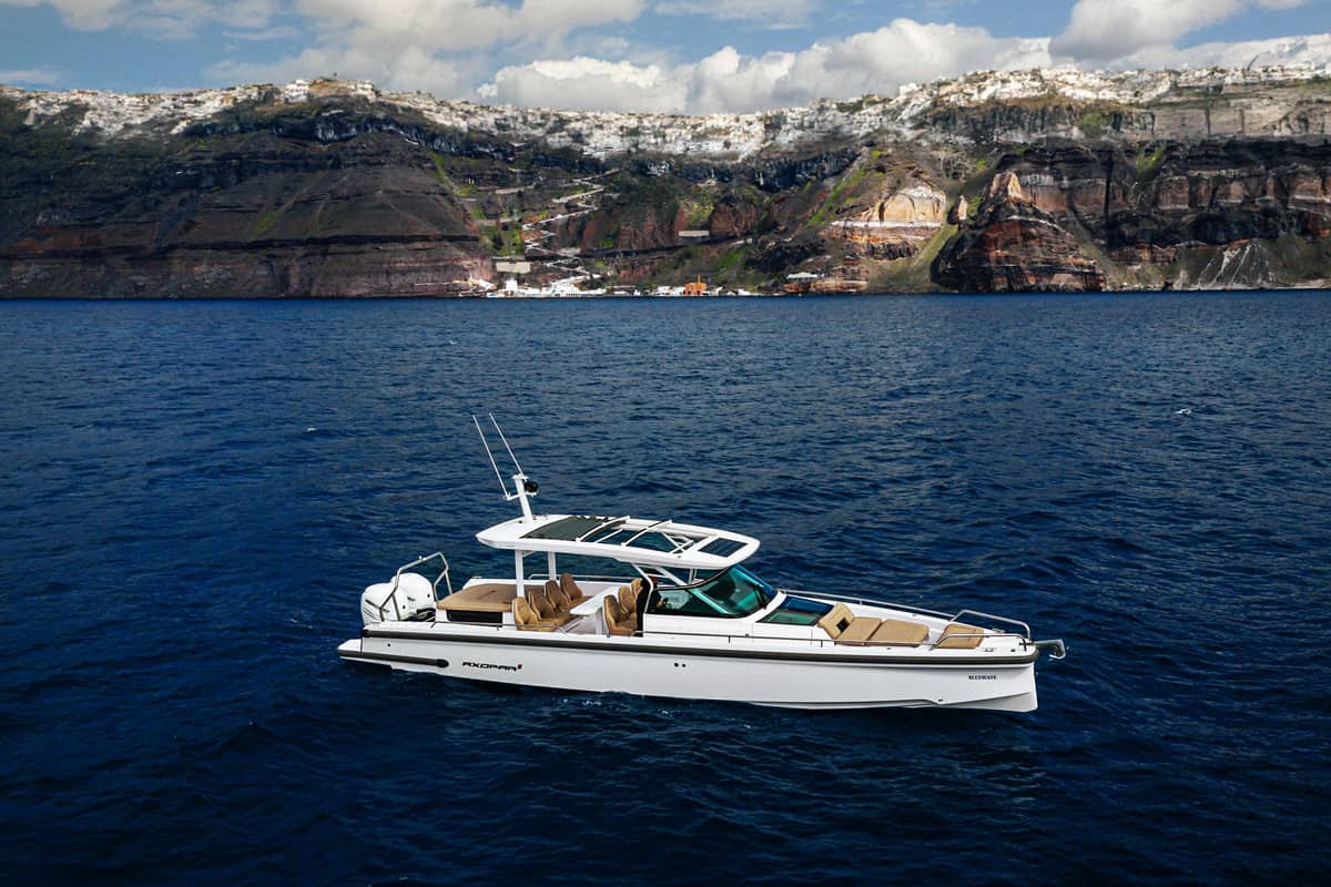 A Santorini yacht cruise motor yacht on deep blue water below the caldera cliffs and the white houses of Fira