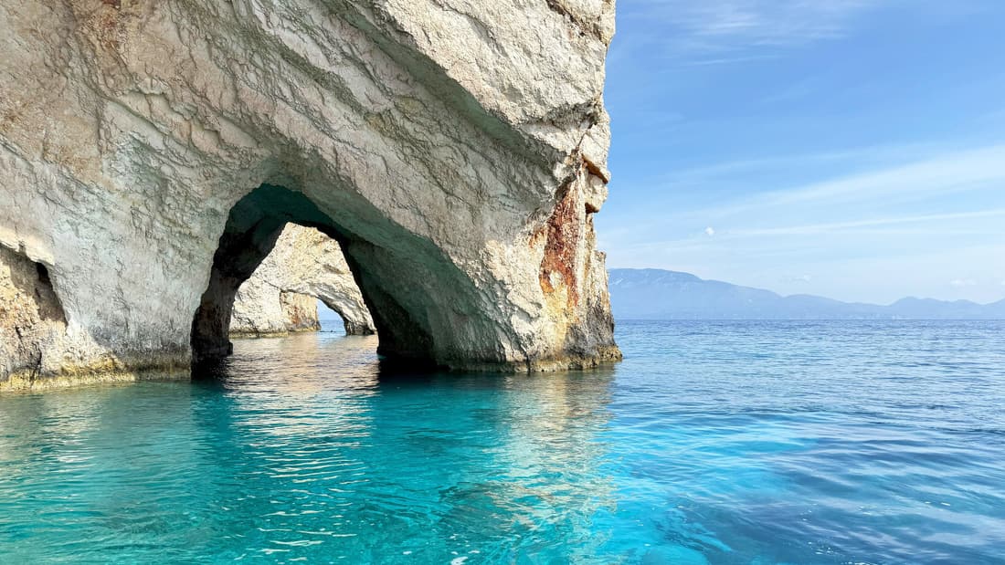 The Zakynthos Blue Caves frame a limestone arch over clear turquoise water at Cape Skinari