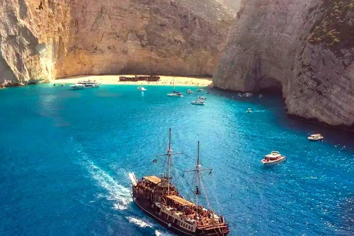 Zakynthos boat trip wooden ship sailing into the blue bay of Navagio, below tall cliffs and the shipwreck beach