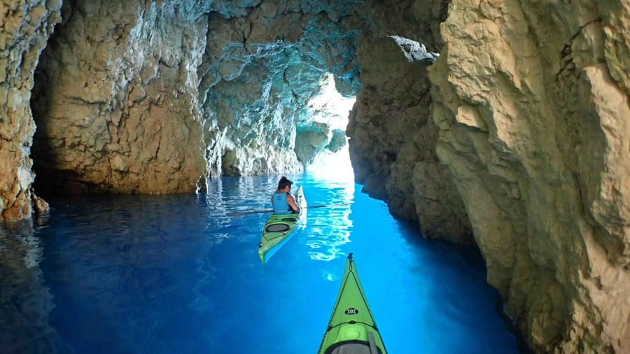 A Zakynthos kayak tour paddles into a sea cave with bright blue water under pale limestone walls