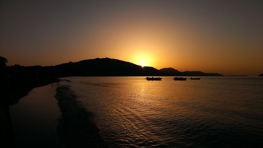 A Zakynthos sunset cruise ends as the sun drops behind the hills and small boats rest on the golden water